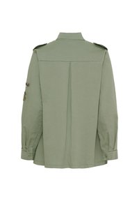 Grön militärtröja i bomull, långärmad, knappade manschetter, axelvaddar, ryggslits, dekorativa lappar på ärmarna.