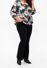 Blusa de estampado floral en tonos de verde, naranja y beige; combinada con pantalones negros acampanados y botas de tacón negras. Mangas largas con bolsillos.