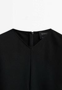 Encolure de robe noire avec fermeture éclair au dos et étiquette visible indiquant "Massimo Dutti Édition Limitée".