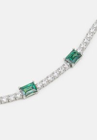Strieborný náramok s dvoma smaragdovo rezanými zelenými kameňmi, ktoré sú lemované okrúhlymi čírymi kameňmi, čím vytvárajú lineárny, textúrovaný dizajn.