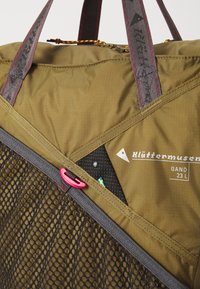 Olivengrønn duffelbag med nettinglomme, grå aksenter, rosa detaljer og logo. Har trekantede mønstre og glidelås.
