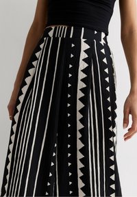 Zwart-witte rok met een patroon van verticale strepen en driehoekige motieven, gemaakt van gerimpeld stof met een aansluitende tailleband.