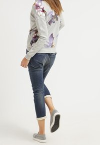 Sweat-shirt gris clair avec imprimé floral sur les manches, assorti à un jean bleu foncé retroussé et des chaussures gris clair sans lacets.