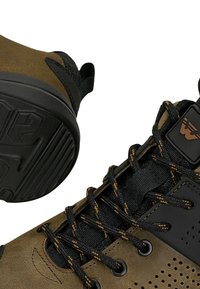 Bottines en suede marron et mesh noir avec une semelle en caoutchouc noir, dotées de lacets orange contrastants et d'un écusson logo, avec des détails perforés sur le côté.
