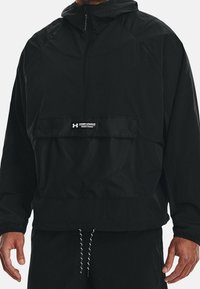 Giacca leggera nera con cappuccio, tasca frontale, cordino regolabile all'orlo e piccolo logo Under Armour sul petto.