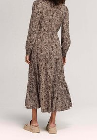 Leopardmönstrad maxiklänning med lång ärm, figursydd midja och flerlagad kjol. Mjukt tyg, rundad halsringning och bärs med beige plattformssandaler.