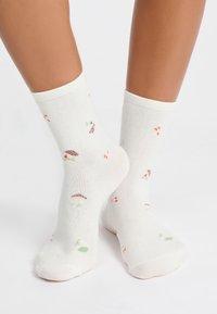 Calzini bianchi in cotone con motivi colorati di funghi, foglie e piccoli punti arancioni e verdi. Lunghezza fino al polpaccio con risvolti a coste.