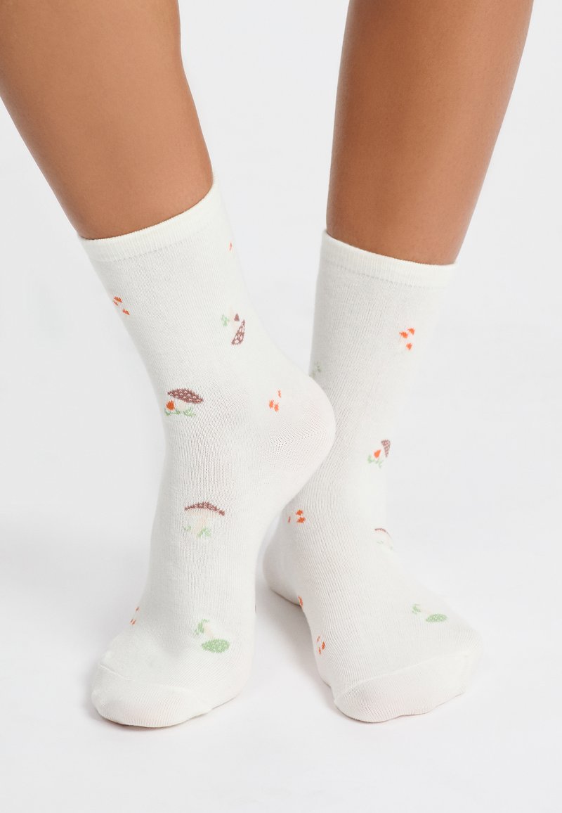 Calzini bianchi in cotone con motivi colorati di funghi, foglie e piccoli punti arancioni e verdi. Lunghezza fino al polpaccio con risvolti a coste.