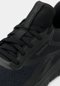 Juodas sportinis batelis su tekstūruotu tinklo viršumi, lygia guma padanga ir toninėmis raištelėmis su subtilia logotipu šone.