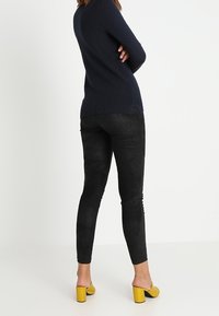 Svart, mocka-liknande leggings med en tät passform och lätt lyster. Matchat med en marinblå, texturerad tröja och gula blockklackade sandaler.