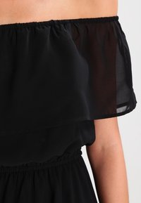 Schwarzes schulterfreies Kleid mit geschichteter, durchsichtiger Oberseite und elastischem Bund. Leichter Stoff mit glatter Textur.