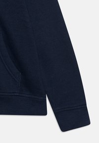 Donkerblauwe sweatshirtmouw met ribbelboord, zachte textuur en geïntegreerde zak aan de zijkant voor functionaliteit.