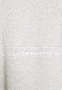 Ljusgrått tyg med vit text tryckt tvärs över mitten där det står "BLI ÖVER DIN HÖJD-RÄDSLA".