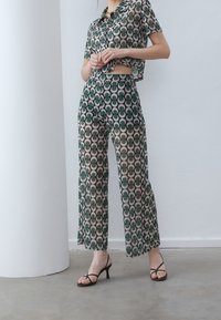 Green and cream patterned two-piece set featuring a cropped short-sleeve shirt and wide-leg pants. The outfit has a smooth, lightweight texture.