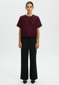 Top bordeaux con texture, dalla vestibilità ampia e maniche corte, abbinato a pantaloni neri a gamba larga e tacchi a punta.