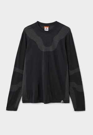 Black long-sleeve shirt with textured patterns, featuring dark grey accents and a triangular logo at the lower left. Smooth fabric finish.