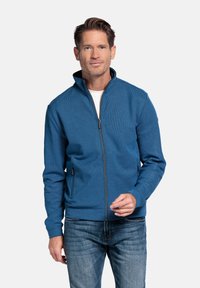 Heren zip-up jas van gestructureerde blauwe stof, met een staande kraag en twee zijzakken, gecombineerd met blauwe spijkerbroek. Soepele afwerking en moderne snit.