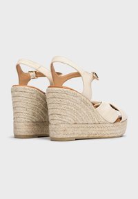 Sandalias de cuña beige con tacón de yute trenzado, punta descubierta y correa al tobillo. Parte superior de cuero suave con un ligero brillo, hebilla ajustable.