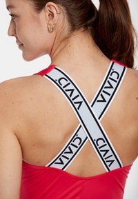 Rotes Sportoberteil mit breiten weißen Trägern und schwarzem Text, entworfen im Racerback-Stil und aus gleitendem Material.