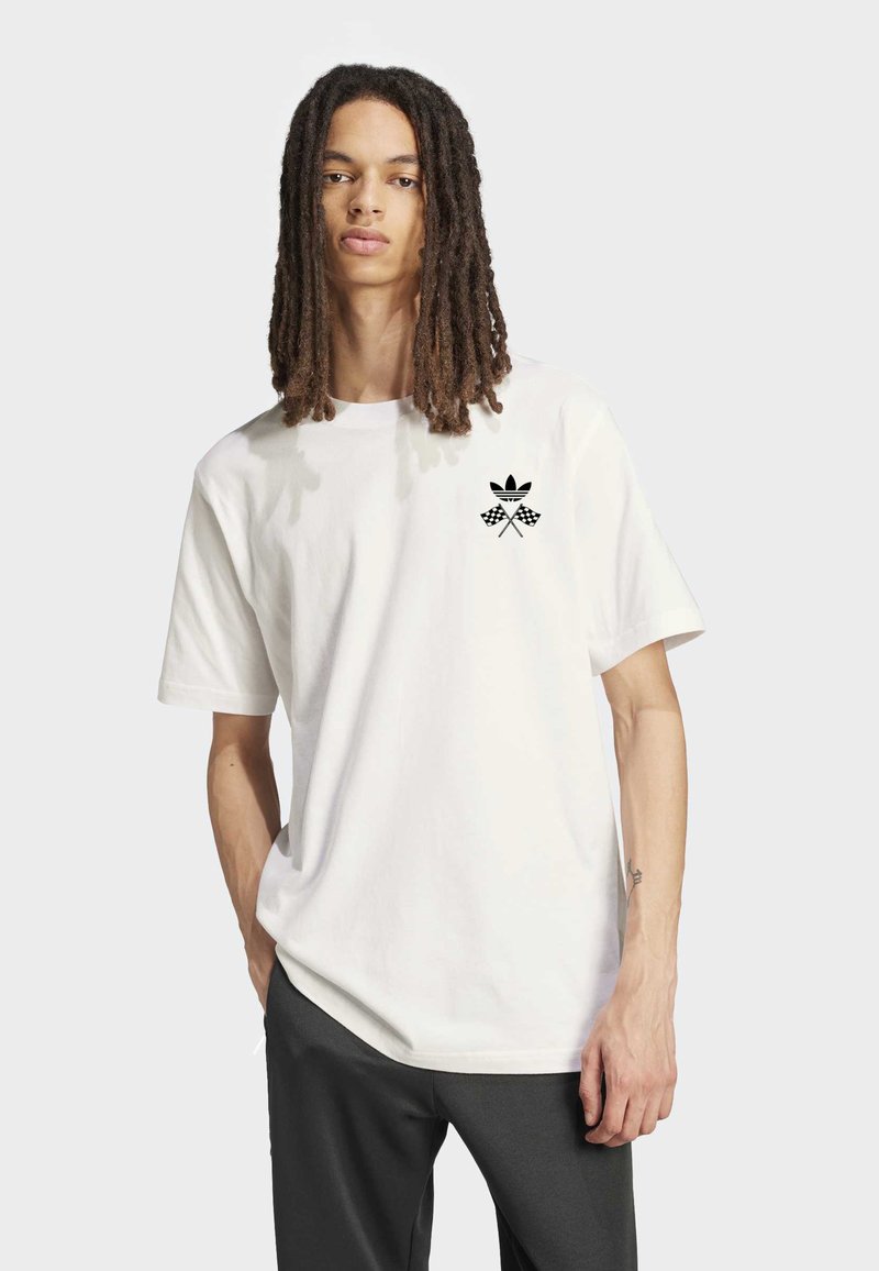 Vit bomullst-shirt med korta ärmar, med en svart grafisk logotyp och korsade rutigvimplar på vänstra bröstet.