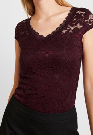 Burgundy lace top with a V-neck and cap sleeves, featuring floral patterns and a textured finish. Paired with black fabric trousers.