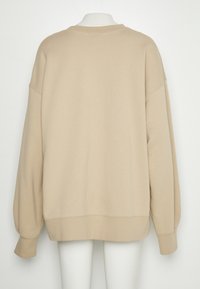 Sweat-shirt oversize beige avec col rond, épaules tombantes et poignets côtelés. Texture douce, détails de couture minimaux visibles.