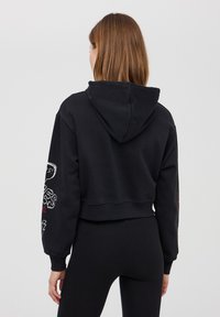 Felpa nera a maniche lunghe con cappuccio, realizzata in tessuto morbido. Presenta stampe grafiche sulle maniche e un orlo a costine. Texture complessiva liscia.