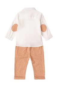 Camisa blanca de manga larga con parches de codo a cuadros naranjas, combinada con pantalones de cuadros naranjas y blancos que cuentan con dos bolsillos traseros.