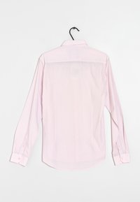 Camicia a maniche lunghe rosa chiaro con collo classico, dettaglio del yoke posteriore e polsini con bottone. Texture liscia, appesa a un gancio nero.