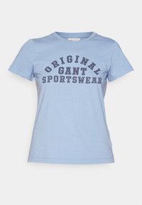 T-shirt di cotone azzurro chiaro con maniche corte, caratterizzato da un design testuale curvo che reca la scritta "ORIGINAL GANT SPORTSWEAR" in blu scuro.