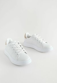 Adidași albi cu o textură netedă, cu șireturi albe, o talpă căptușită și un accent bej deschis la călcâi. Design simplu, fără modele.
