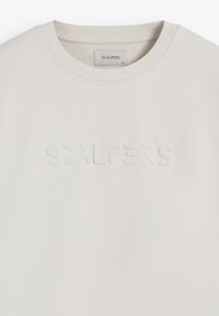 Sweat-shirt beige clair avec un logo texturé en relief "SCALPERS" sur la poitrine. Présente un col côtelé et un tissu doux.