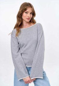 Gray long-sleeve top with a boat neckline and white trim. Soft ribbed texture, relaxed fit, paired with light blue jeans.