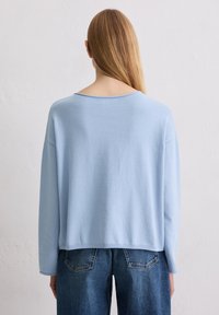 Hellblauer Pullover mit langen Ärmeln, lockerem Schnitt und tiefem Rückenausschnitt, kombiniert mit hoch taillierten Jeans. Weiche Textur und entspanntes Design.
