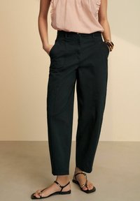Pantalons en coton noir à coupe décontractée, taille mi-haute et poches latérales. Associés à des sandales noires fines et un haut rose clair.