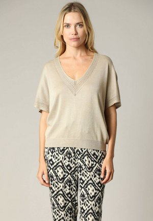 Haut beige en tricot à manches courtes avec un décolleté en V et des détails en dentelle intricats. Associé à un pantalon à motifs noir et blanc avec des formes de losanges.