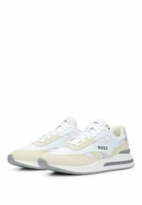 Paire de baskets BOSS blanches et beiges avec des accents gris, design à lacets, et semelle et côtés marqués du logo, positionnées en angle sur fond blanc.