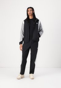 Black and gray tracksuit with a zip-up jacket and elastic waistband pants. Notable design includes contrasting sleeves and logo detail.