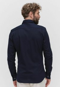 Marineblauwe overhemd met lange mouwen, kraag, detail van een rugpand en knoopmanchetten. Gladde stof met een getailleerde pasvorm en afgeronde zoom.