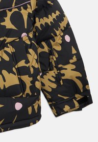 Μανίκι μαύρου μπουφάν puffer με έντονο, αφηρημένο χρυσό και ροζ σχέδιο, με τσέπη με φερμουάρ και υφή στο ύφασμα.