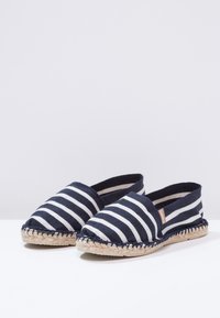 Gestreifte Espadrilles aus marineblauem und weißem Canvas mit einer Sohle aus Jute. Rutschfeste Ausführung, runde Zehenpartie und elastische Akzente an den Öffnungen.