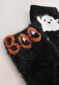 Zwarte, pluizige sokken met het woord "BOO" in oranje en een wit spookontwerp, met een zachte textuur en een speels Halloween-thema.