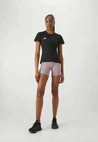 Čierne športové tričko s krátkymi rukávmi a bielym logom, v kombinácii so svetlo levanduľovými šortkami. Model má na sebe čierne tenisky. Hladká štruktúra látky.