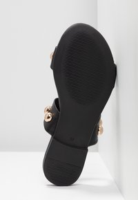 Black sandal featuring a textured sole, rounded gold studs as accents, and a wide strap design. Size marked as 37.