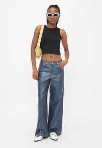 Black cropped tank top, wide-leg blue denim jeans, white shoes with black accents, green bag, and white sunglasses. Smooth textures and casual fit.