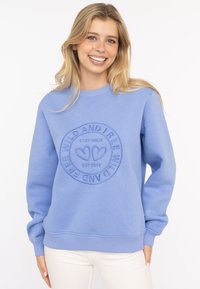 Jasnoniebieski sweatshirt z okrągłym dekoltem, wykonany z miękkiego materiału, z wytłoczonym okrągłym logo z sercami oraz napisem "STAY WILD" i "EST 2014".