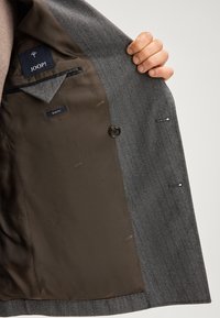 Blazer grigio a righe con fodera in satin marrone. Presenta un'etichetta slim fit, chiusura con bottone e tasche interne.