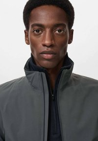 Grijze zip-up jack met hoge kraag, gemaakt van gladde stof, met een contrasterende donkere binnenvoering en subtiele textuurdetails.