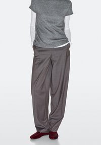 Pantaloni grigi a vita alta con vestibilità ampia, maglia a maniche corte in tessuto testurizzato grigia, sovrapposta a una camicia bianca aderente a maniche lunghe.