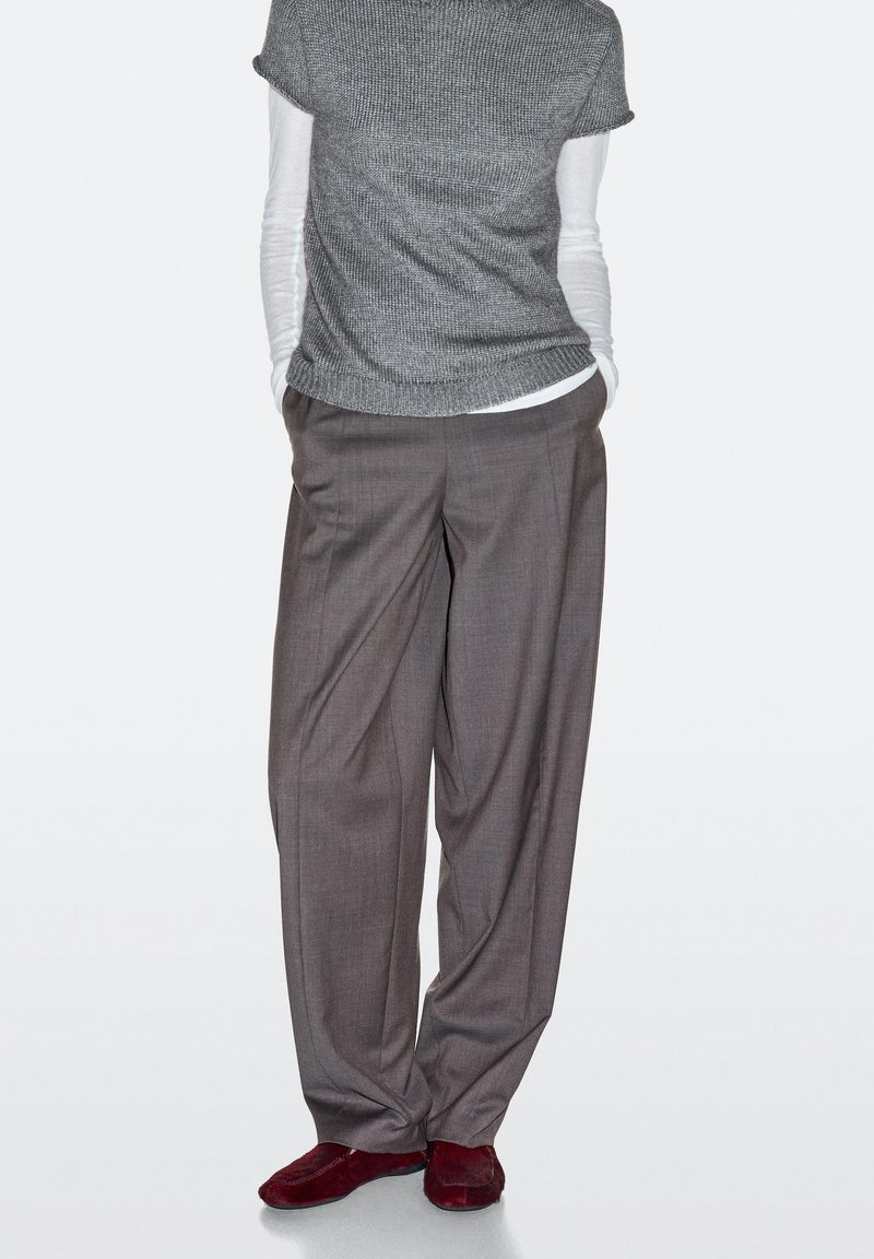 Pantaloni grigi a vita alta con vestibilità ampia, maglia a maniche corte in tessuto testurizzato grigia, sovrapposta a una camicia bianca aderente a maniche lunghe.